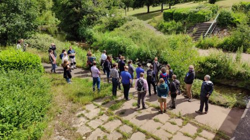 A large group of people at the conference. They are standing next to a river and watching the presenter speak