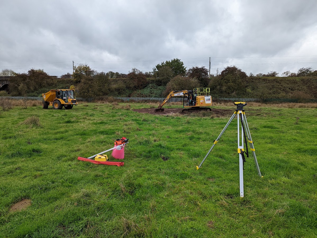 Surveying equipment in a field with diggers in the background