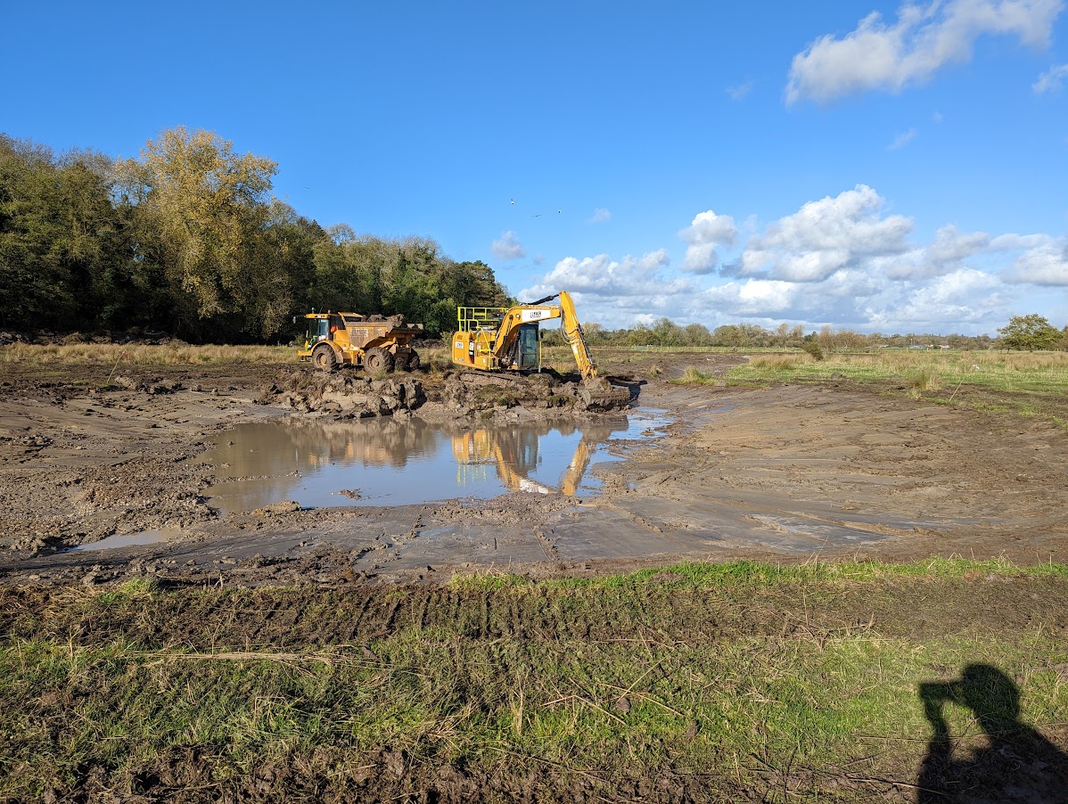 A digger working on creating a shallow pool of water in the middle of a large field